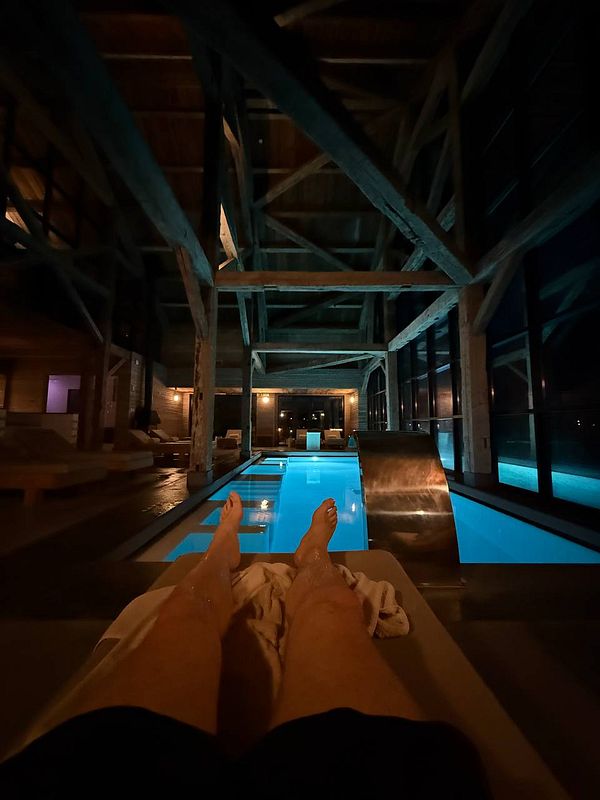 A person relaxes by a modern indoor pool in a wooden structure at night.