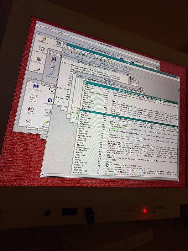 A vintage Windows 3.11 interface displayed on a monitor, showcasing multiple overlapping windows and a red patterned background.