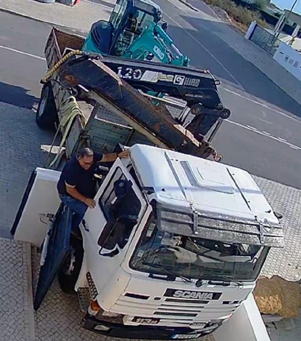 A truck driver is seen attempting to maneuver a large truck near a damaged electric gate.