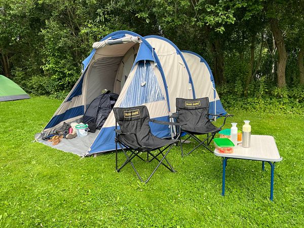 A camping setup featuring a tent, chairs, and a small table in a grassy area.