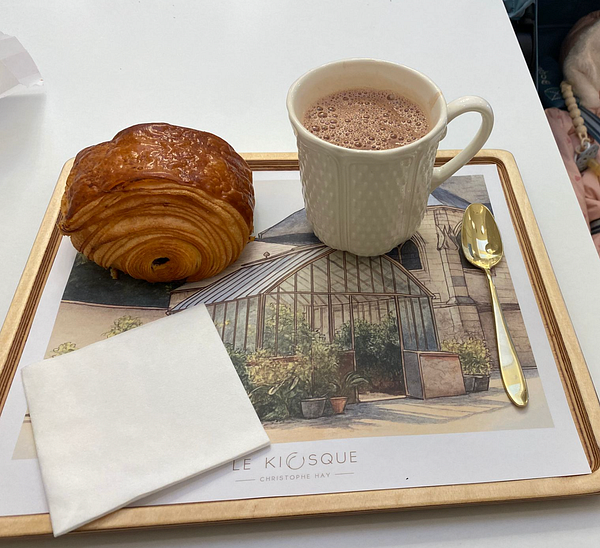 A cozy breakfast setup featuring a croissant and a cup of hot chocolate on a decorative tray.