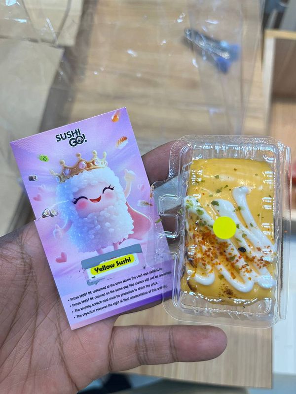 A hand holds a prize card and a piece of yellow sushi from a promotional scratch-and-win game.