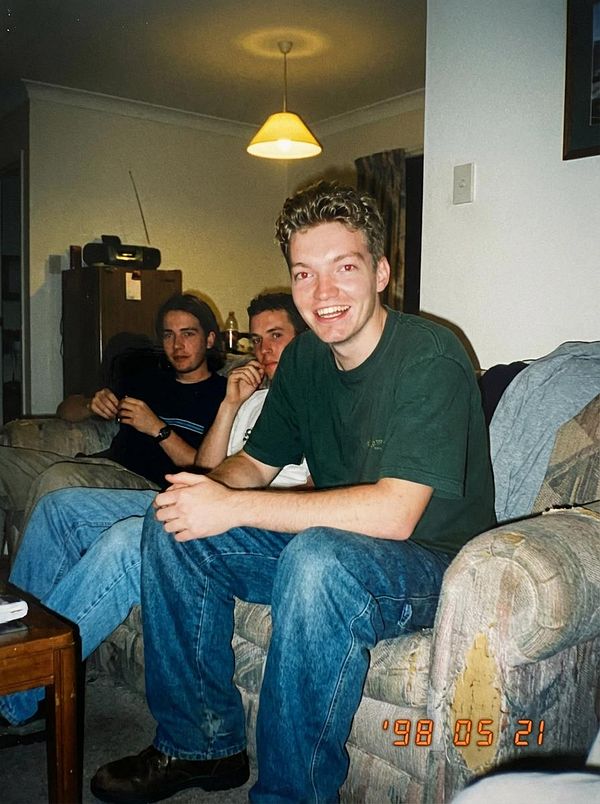A group of three young men are sitting on a couch in a casual living room setting.