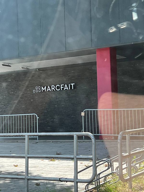 The image features the exterior of a building with the name 'MARCFAIT' prominently displayed.