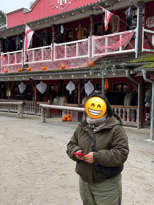 Person standing in front of a red wooden western-style building decorated with pumpkins and ghost decorations.