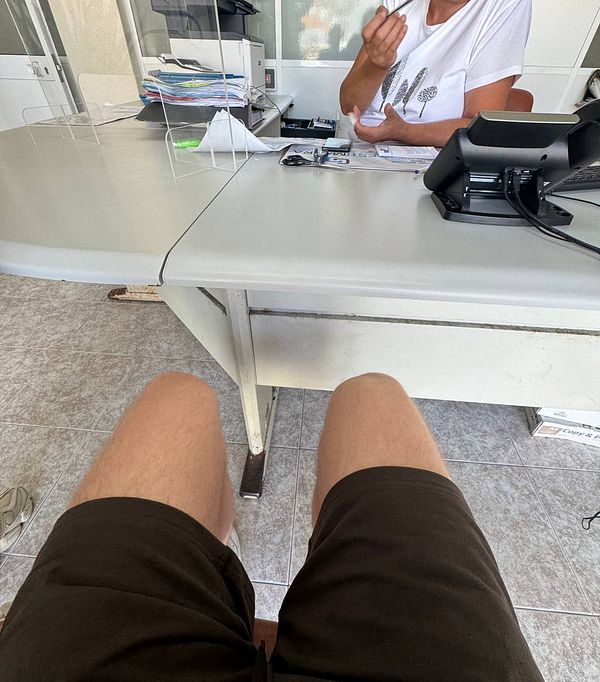 A person is seated at a desk in a driving school office, preparing to sign up for a theory exam.
