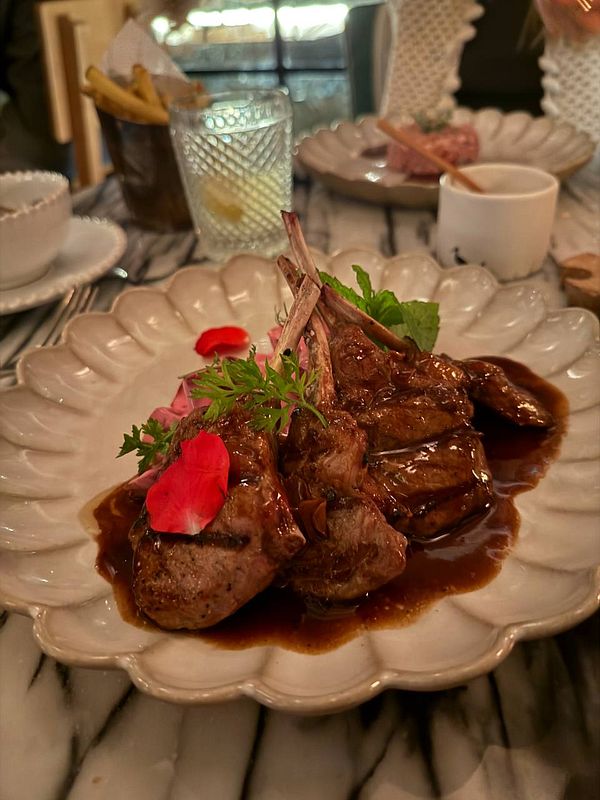 A beautifully plated dish featuring lamb chops garnished with herbs and rose petals.