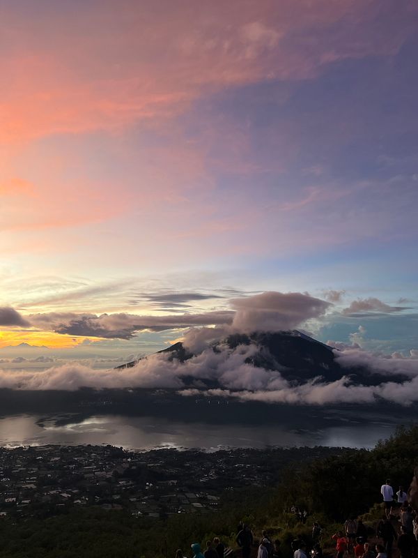 A breathtaking view of Mount Batur at sunrise, surrounded by clouds and a serene landscape.