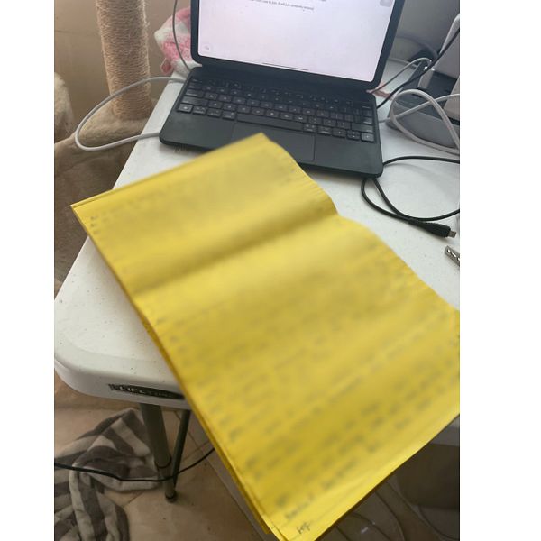 A yellow notebook is open on a table next to a laptop.