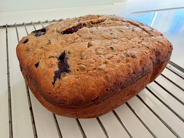 A freshly baked banana cake with visible blueberries cooling on a wire rack.