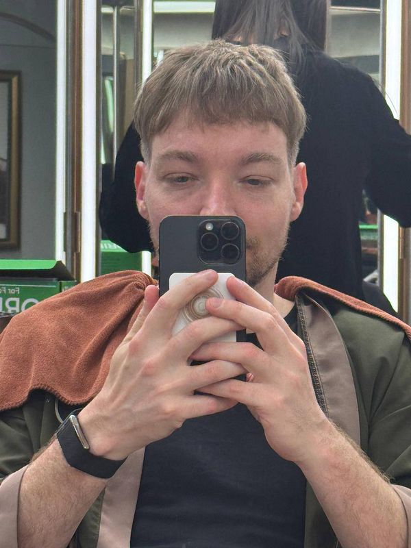 A man is taking a selfie in a barber shop, showcasing his new haircut.