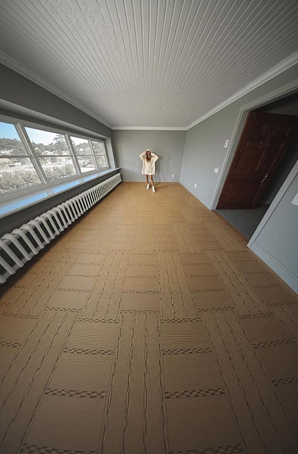 A spacious, empty room with a woman in a light-colored outfit standing in the center.