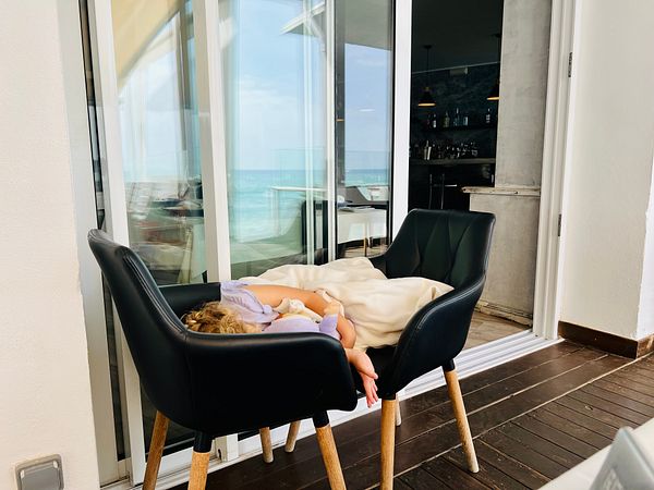 A young girl is comfortably resting in a chair at a beach restaurant.