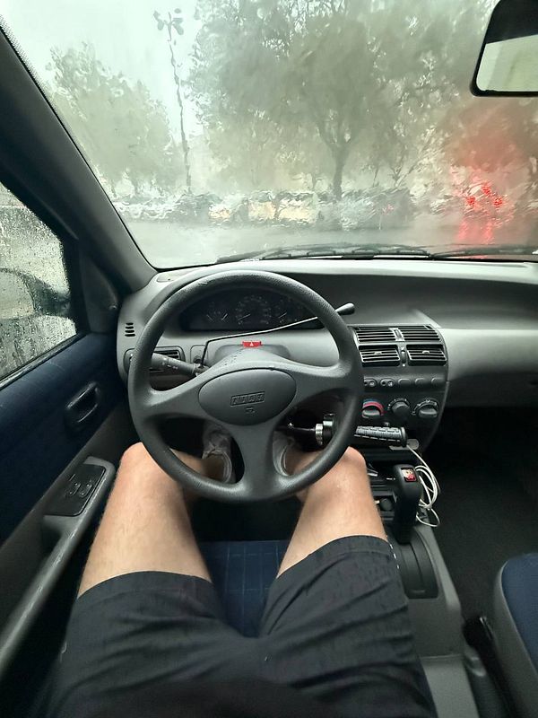 The image captures the interior of a car during a rainy day, focusing on the driver's perspective.