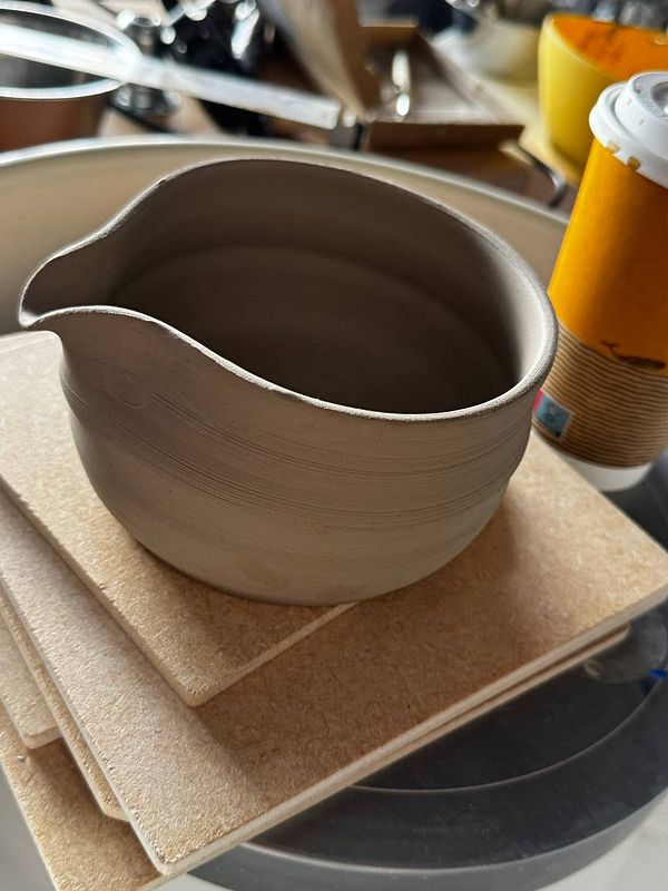 A pottery wheel in use with hands shaping clay inside a workshop studio.