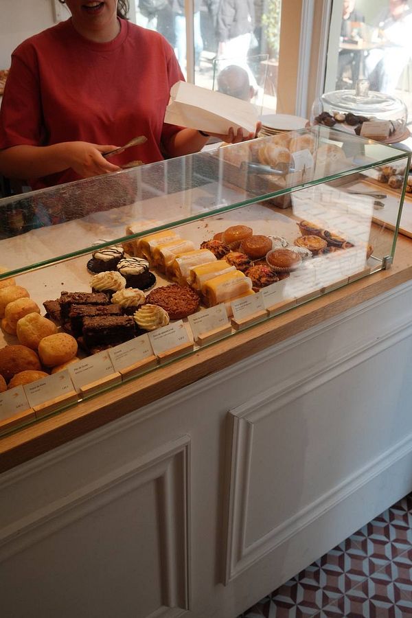 A bakery display featuring a variety of Portuguese pastries and a smiling employee.