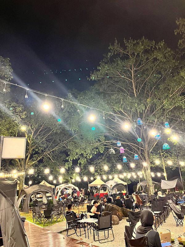 A vibrant outdoor camping cafe scene at night, filled with people enjoying the ambiance.