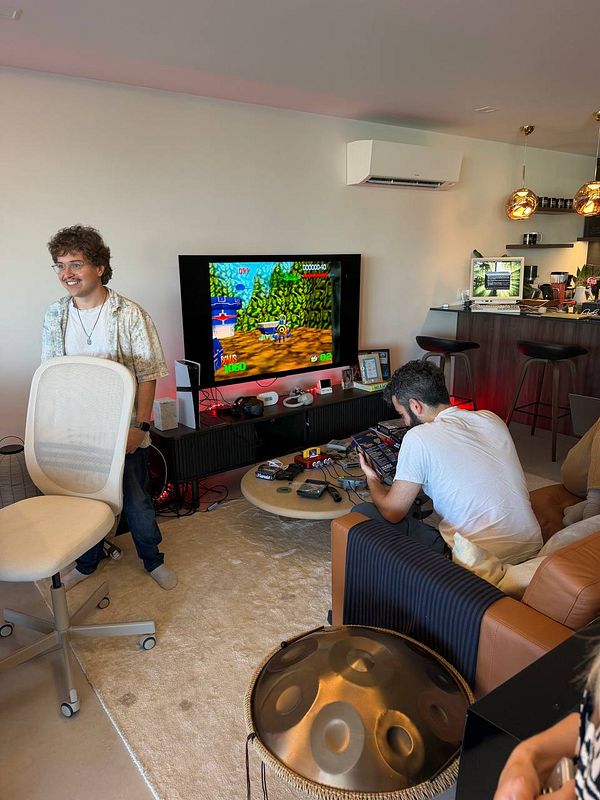 A modern living room setup with two men, a TV displaying a retro video game, gaming consoles, and a cozy lounge area.