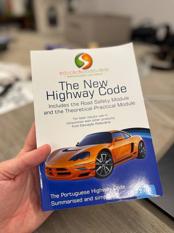 A person is holding a driving school textbook titled 'The New Highway Code'.