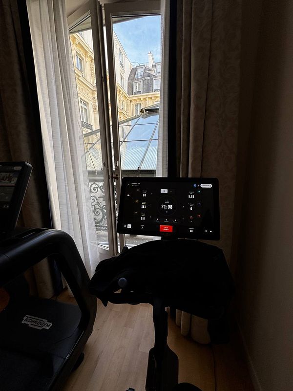 A view from inside a gym with a stationary bike and an open window overlooking a Parisian courtyard.