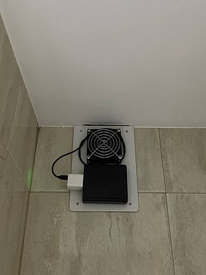 A mounted ventilation system with a fan and power supply is installed on a wall.