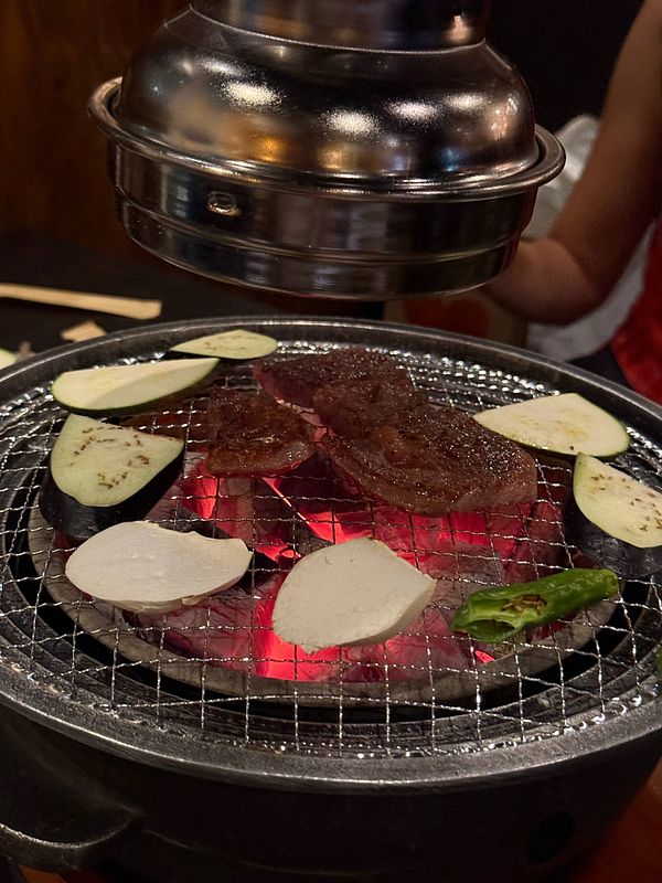 Korean BBQ grill with Hanwoo beef and vegetables cooking over hot charcoal.