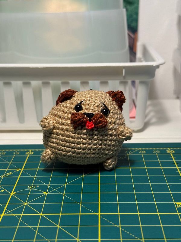 A crocheted critter resembling a small, round dog with a playful expression.