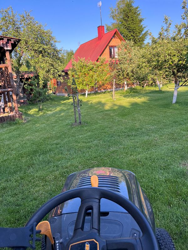 A view from a riding lawn mower in a lush green yard with a family home in the background.