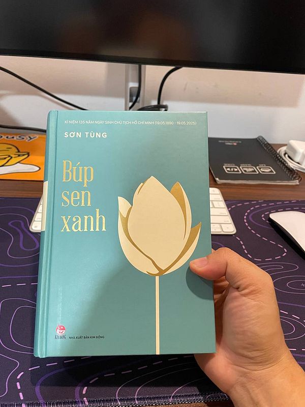 A person is holding a book titled 'Búp sen xanh' by Sơn Tùng, with a light blue cover featuring a lotus design.