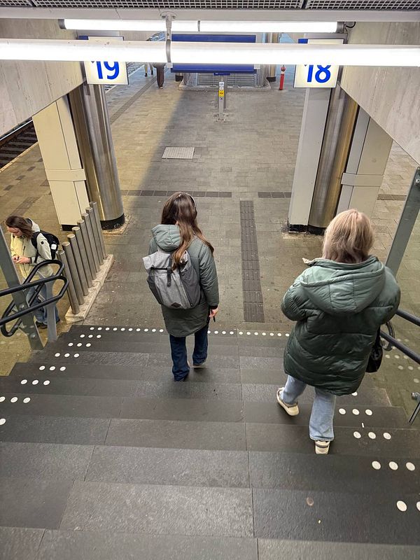Two individuals are descending a staircase in a train station.