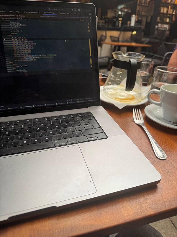 A laptop displaying code is set on a wooden table alongside a coffee cup and a coffee carafe.