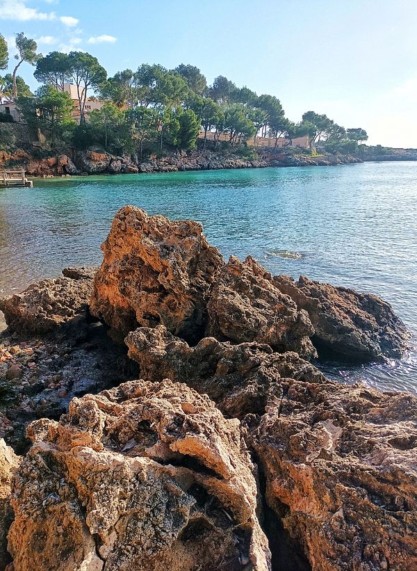 A scenic view of rocky shoreline and clear blue water under a bright sky.