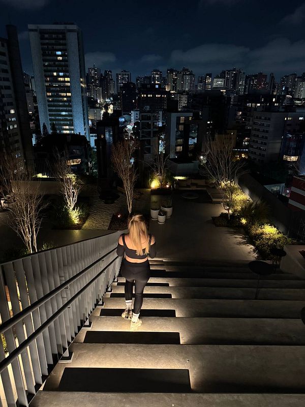 A woman walks down illuminated stairs at night, with a city skyline in the background.
