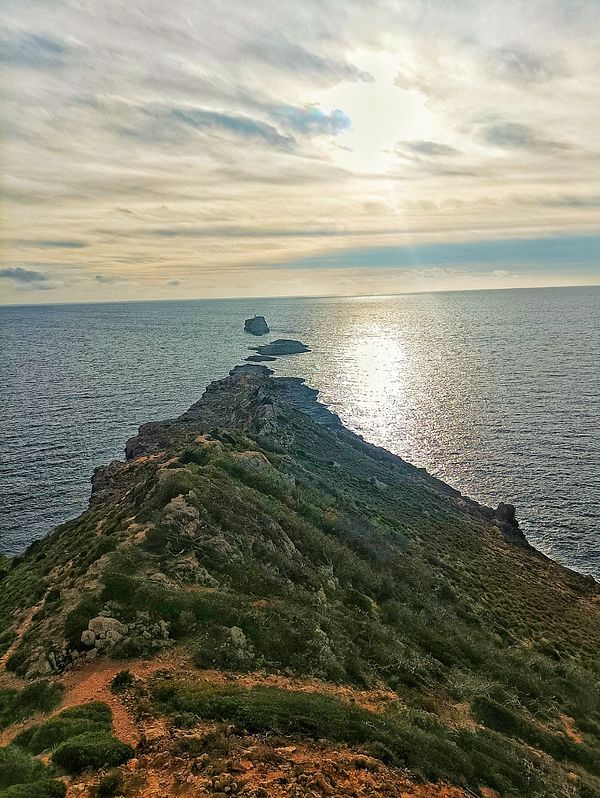 A scenic coastal view featuring a rocky peninsula extending into the ocean under a cloudy sky.