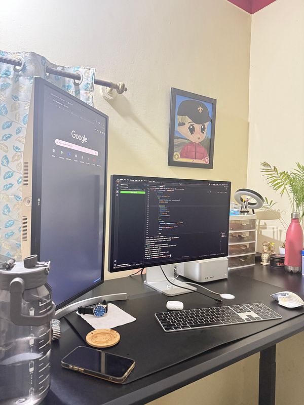 A cluttered desk setup featuring two monitors, a water bottle, and various desk items.