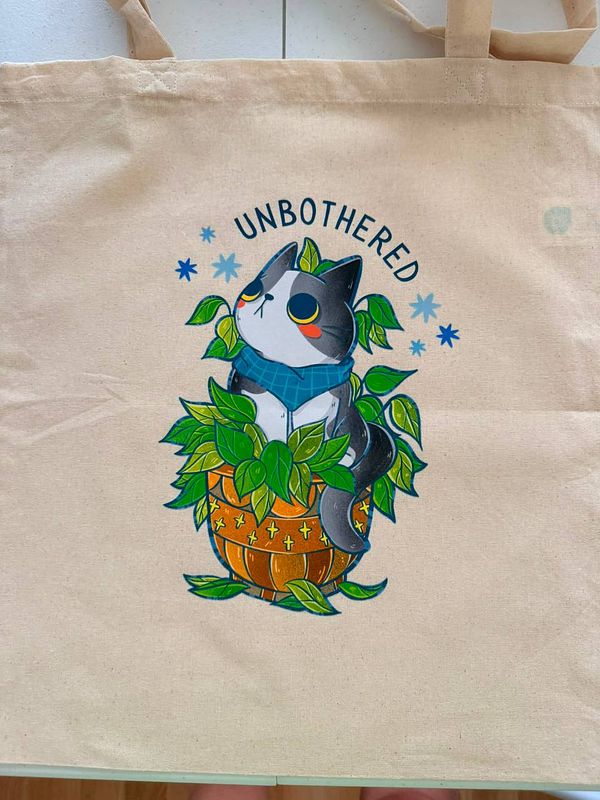 A wooden table displays various colorful enamel pins and printed tote bags arranged neatly for product showcasing.