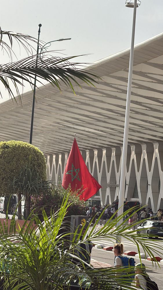 An aerial view over Marrakesh showing lush green golf courses, residential buildings, and a backdrop of distant mountains under a bright sky.