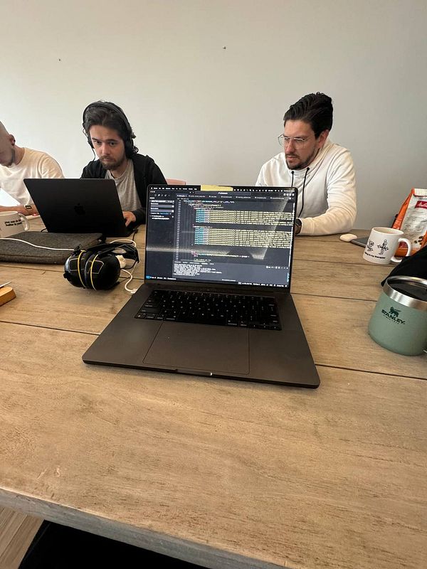 A group of individuals is engaged in a coworking session at a table with laptops and snacks.