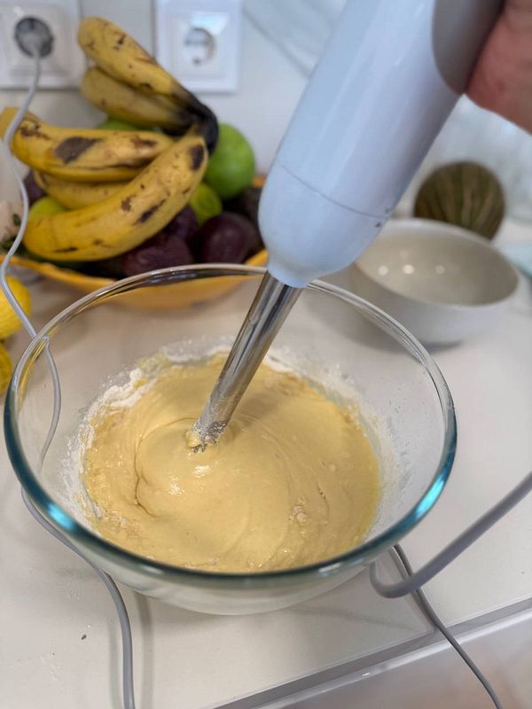 A person is mixing cake batter in a glass bowl with a hand mixer.