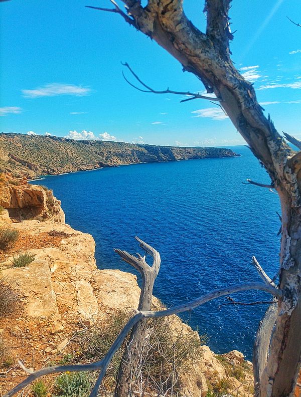 A scenic coastal view featuring rocky cliffs and a vibrant blue sea under a clear sky.