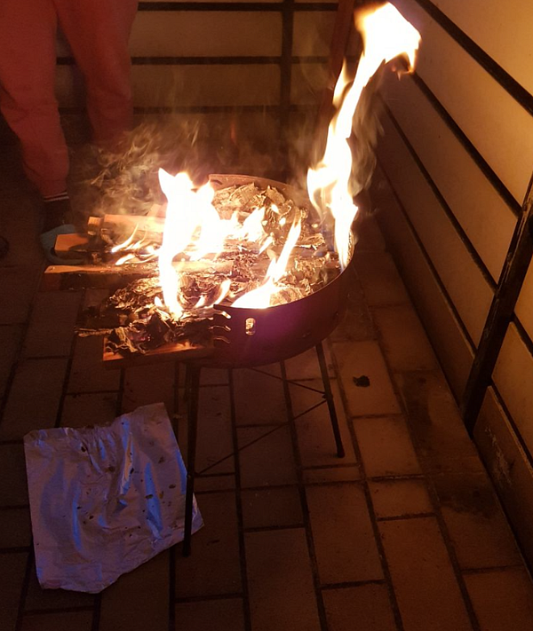 A fire burns brightly in a metal grill, surrounded by a cozy outdoor setting.