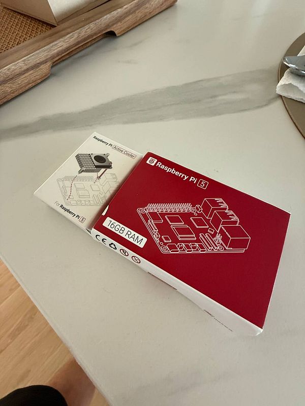 The image features a Raspberry Pi 5 package alongside an active cooler package on a countertop.