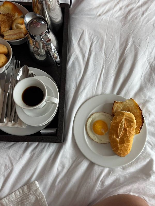 A cozy breakfast tray is set on a bed, featuring a variety of food items and a cup of coffee.