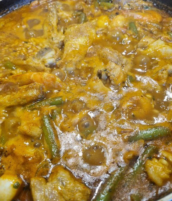 A close-up view of a simmering paella dish filled with various ingredients.