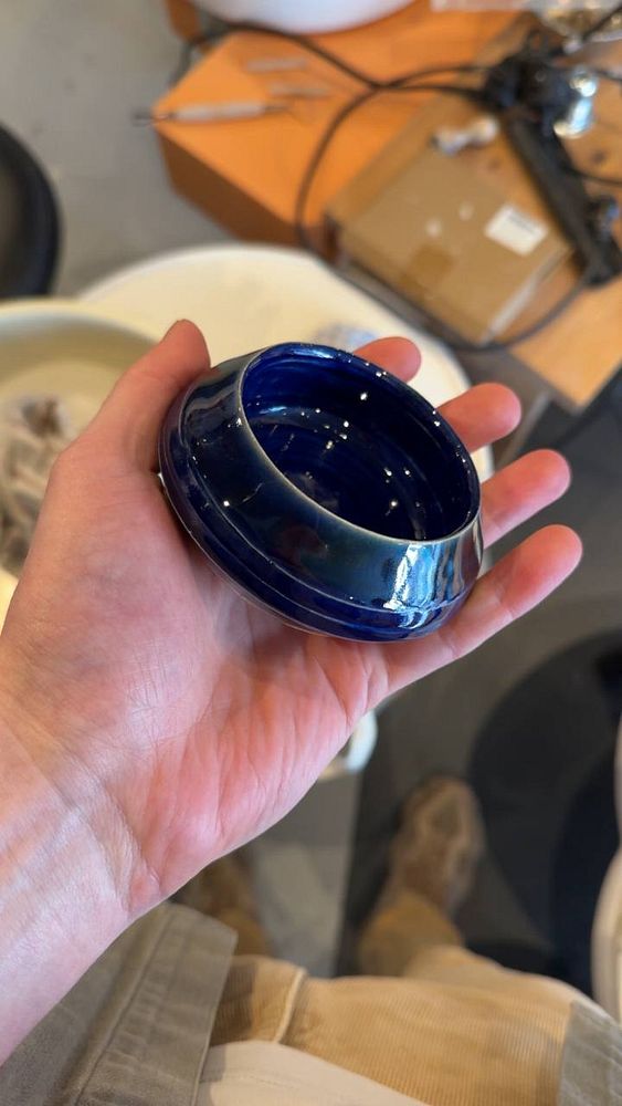A young woman is engaged in pottery making, shaping clay on a pottery wheel in a workshop setting.