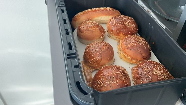 Freshly baked sesame seed buns and a bread roll cooling on a tray, showcasing home bread baking efforts.