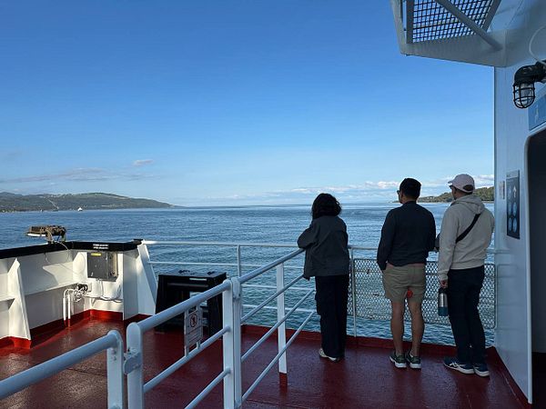 Three friends enjoy a scenic view from the deck of a ferry.