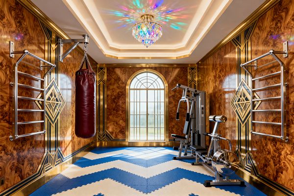 A luxurious Art Deco home gym with glossy burled wood wall panels trimmed in gold geometric inlays and a gilded arched window at the far end. A prismatic crystal chandelier and cove lighting scatter rainbow reflections over royal blue and cream chevron foam flooring. Stainless steel stall bars, a burgundy leather heavy bag, a multi-gym station, and a chrome rower complete the setup.