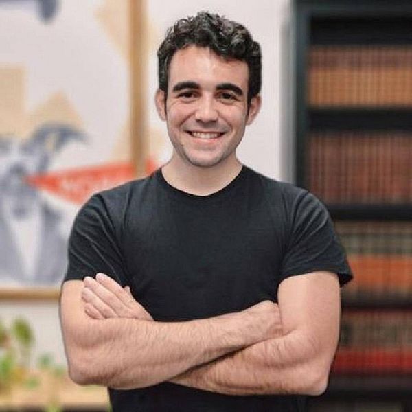 A young man stands confidently with his arms crossed, smiling at the camera.