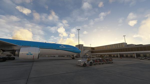 A KLM airplane is parked at an airport with a clear sky and terminal in the background.